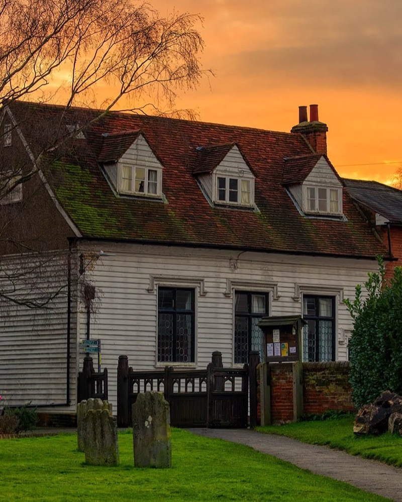 A weatherboarded cottage beside the churchyard at sunset